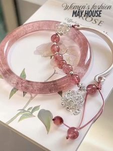 Vòng tay thạch anh hồng kết hợp với chuỗi hạt và charm bạc phong thủy, đặt trên nền sách hoa